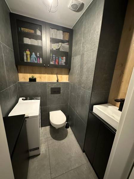 Bathroom with toilet in a 2-room apartment, tiles, cabinet, washing machine, and storage space.