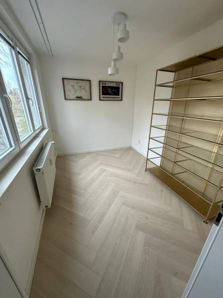 A room in a 2-room apartment with a shelf, a wooden decor floor, and a window.
