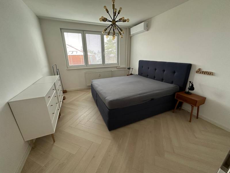 Bedroom with a bed, white dresser, wood-patterned floor, and pendant light.