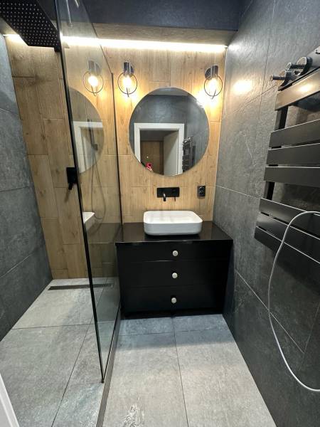 Bathroom in a 2-room apartment with a sink on a black cabinet table and a round mirror.