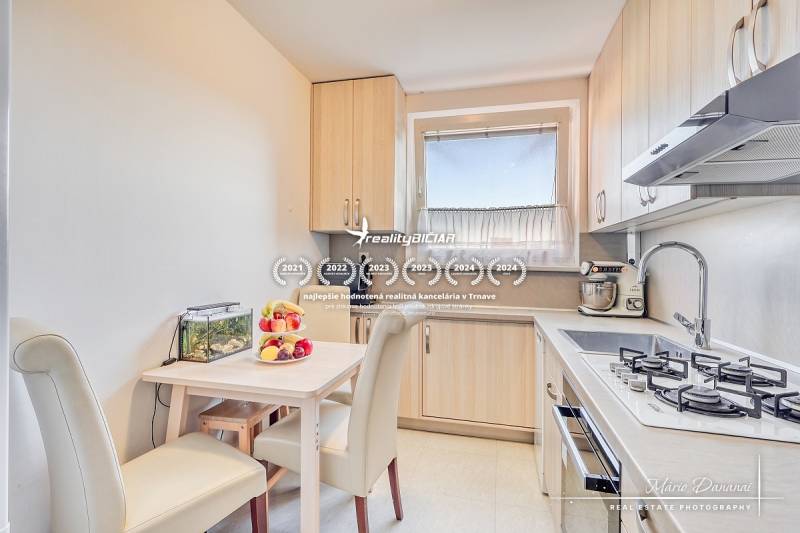 A kitchen in a 4-room apartment with a dining table, cream chairs, and a kitchen unit.