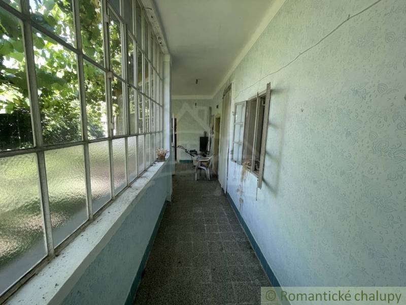 A narrow glass-enclosed space in a family house with a view of the garden.