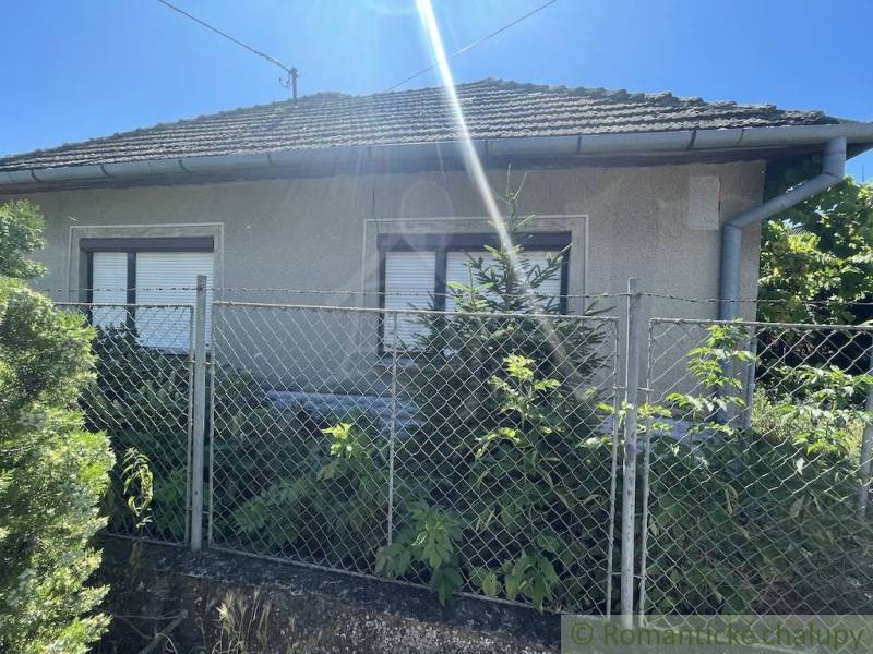 A family house in Tvrdošovce with a fence and greenery, under a clear sunny sky.
