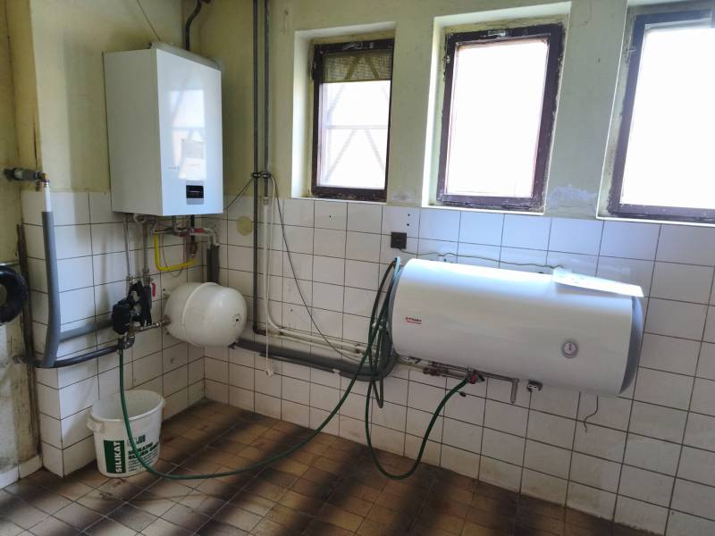 Boiler room in a family house with a gas boiler and a water heater, white tiles on the walls.