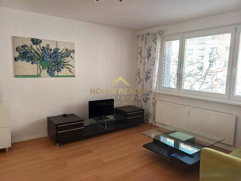 Living room with wood-patterned flooring in a three-room apartment, includes a television and a table.