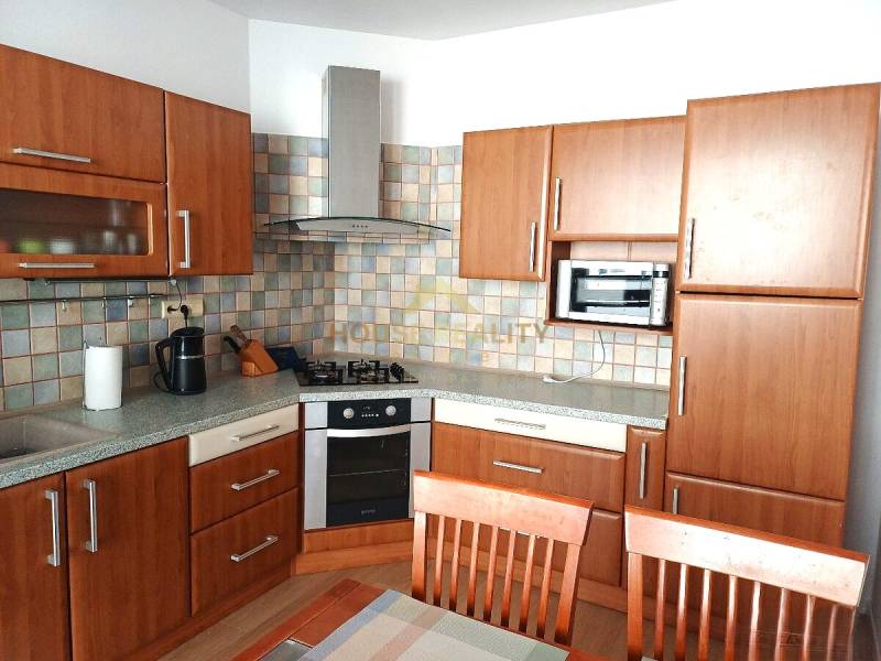 A kitchen in a 3-room apartment with a wood-patterned floor and kitchen cabinets.