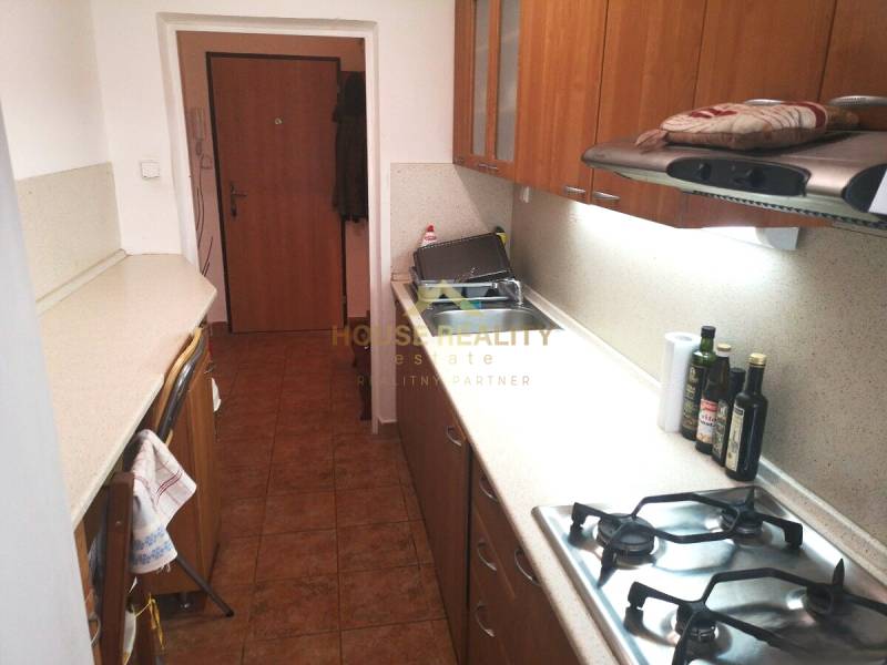 A kitchen in a 2-room apartment with a gas stove and wooden decor cabinets.