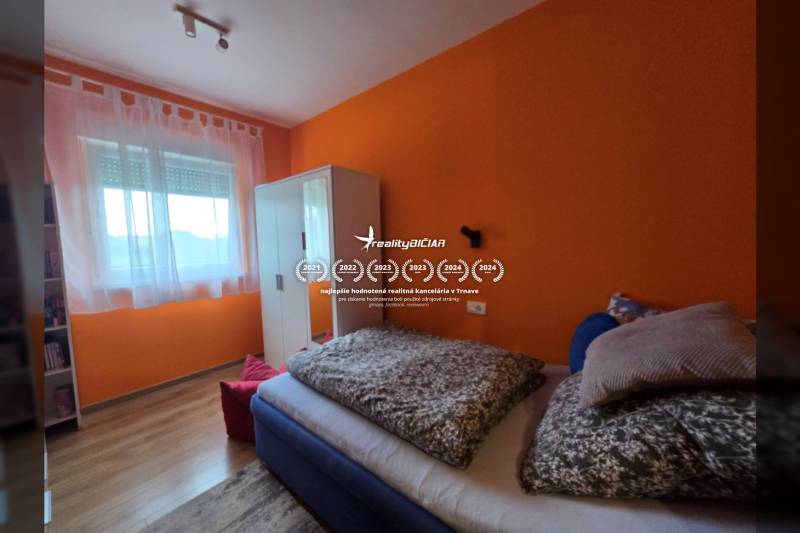A bedroom in a holiday apartment with a bed, orange walls, and a wood-patterned floor.