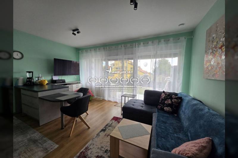 Living room in a holiday apartment with wood-patterned flooring, a sofa, and a TV.