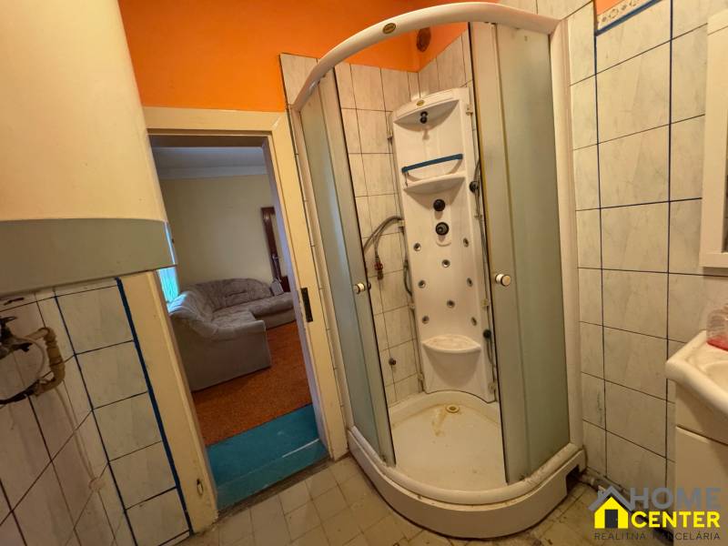 A bathroom with a hydromassage shower in a family house, visible living room with a sofa.