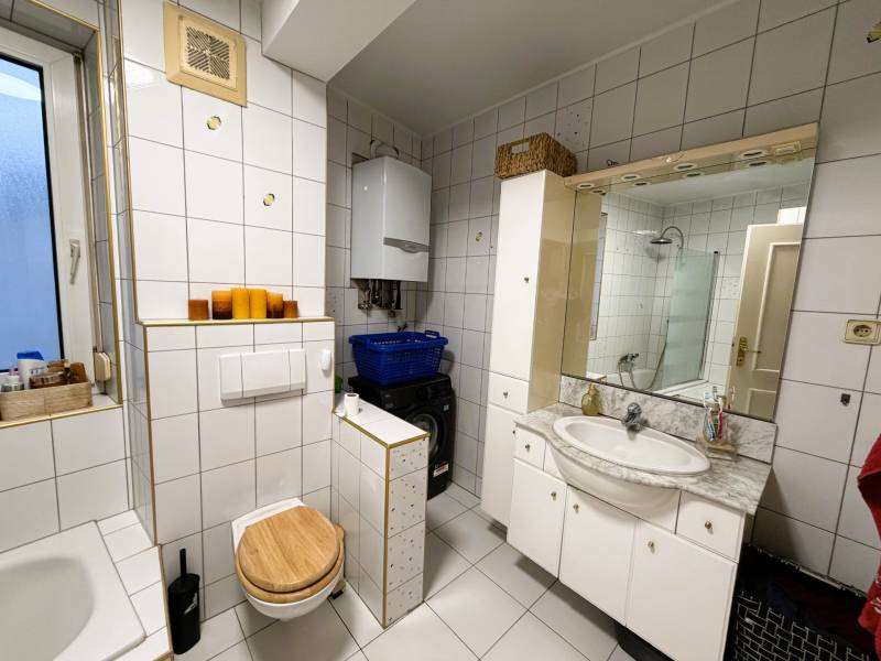 Bathroom in a 3-room apartment with a bathtub, toilet, and washing machine, white tiles.
