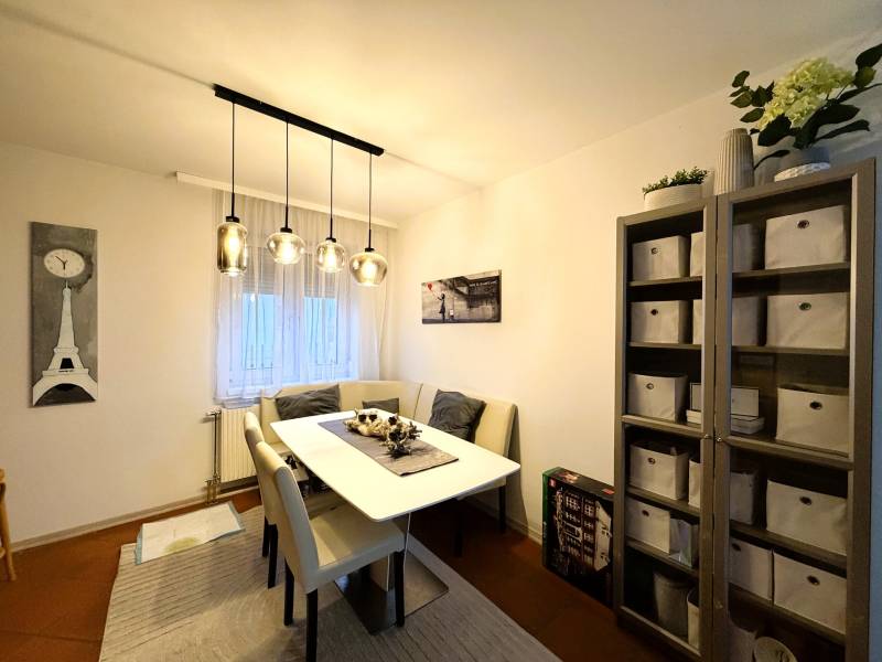 A dining room with a table, chairs, and a shelf in a 3-room apartment with decorative lighting.