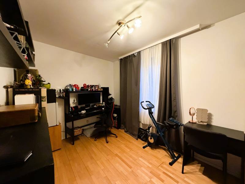 A room with a wood-patterned floor, a desk, a computer, a stationary bike, shelves.