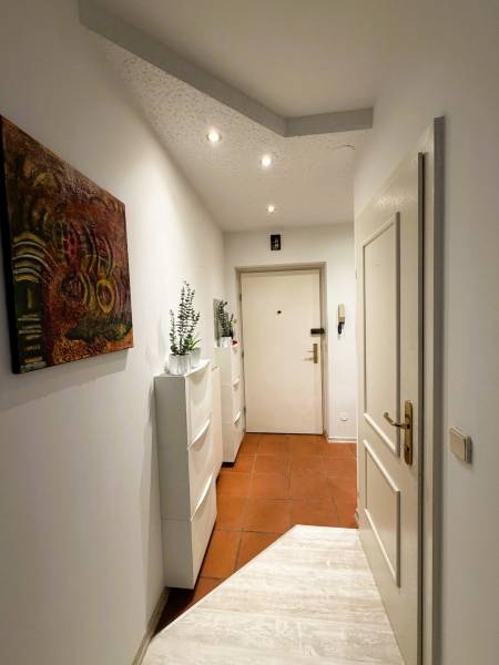 A hallway in a 3-room apartment with white furniture and a painting on the wall.