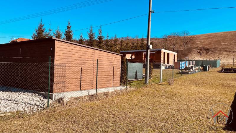 Construction of houses in Prosačov, Prosačov: fence, wooden structure, trees, and blue sky.