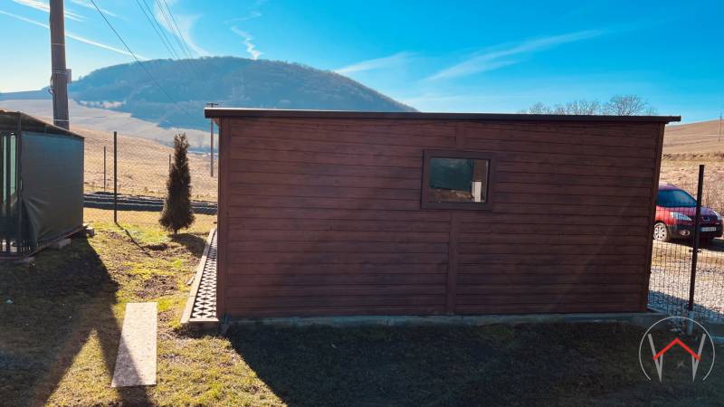 A small wooden house on the street in Prosačov with a view of the hills and blue sky.