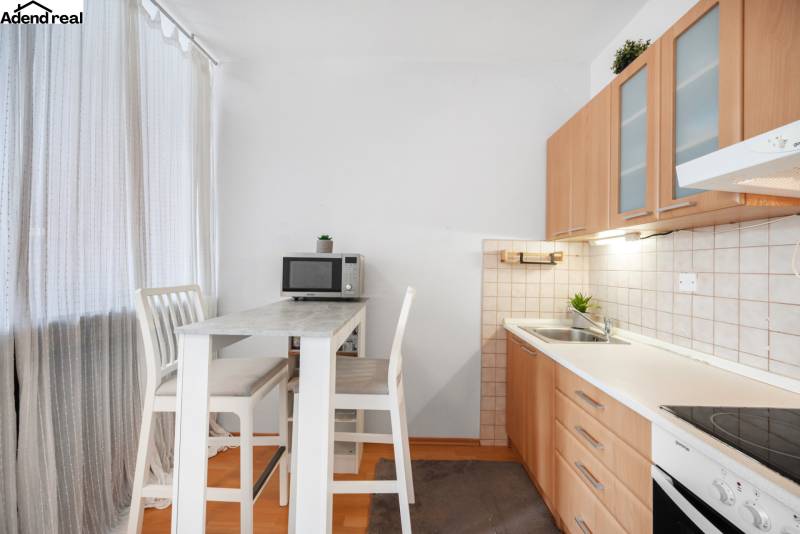 Kitchen in a studio apartment with a bar table, chairs, and a kitchen unit.