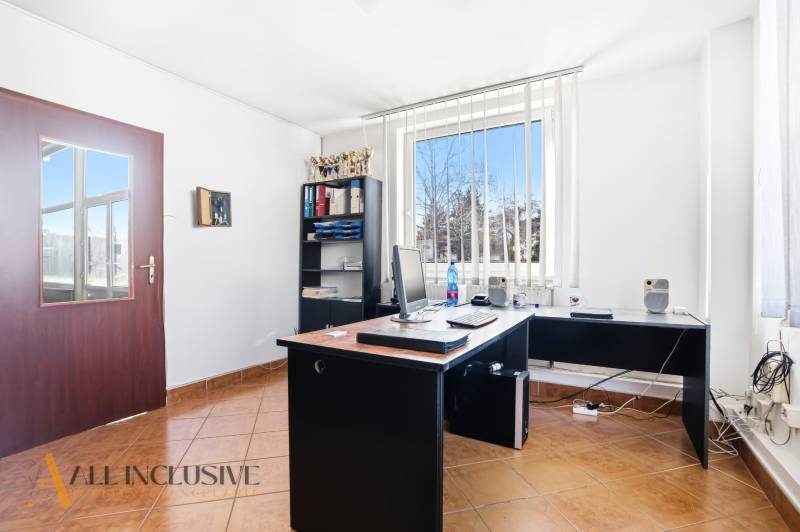An office with a computer, a shelf, and a window with vertical blinds in commercial premises.