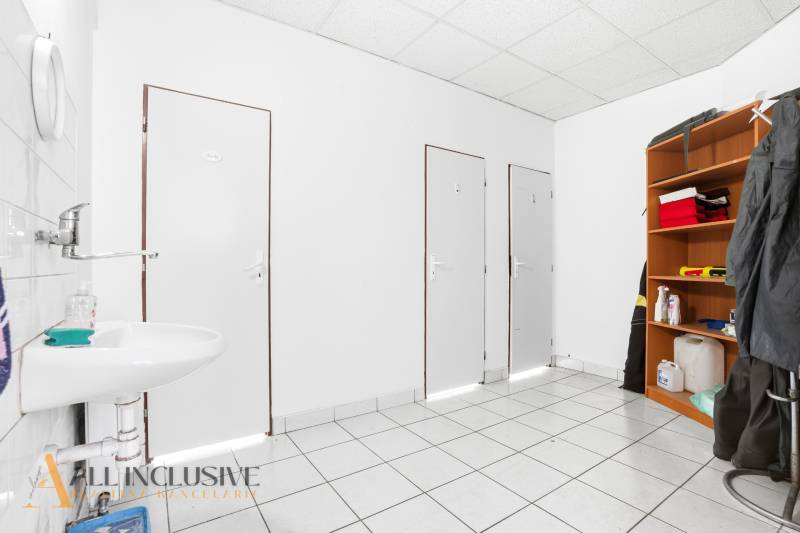 Bathroom with a sink, tiles, door, and shelves with cleaning products in commercial premises.