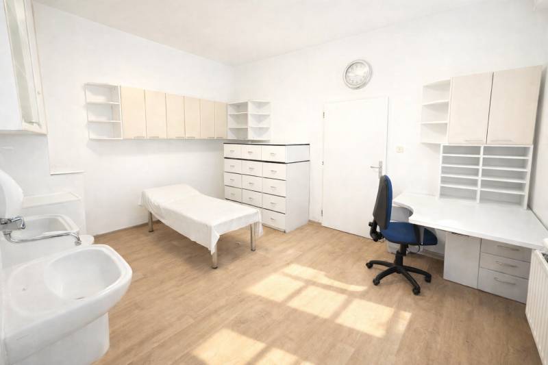 A white office with a sink and wood-patterned flooring, furnished with a desk and cabinets.