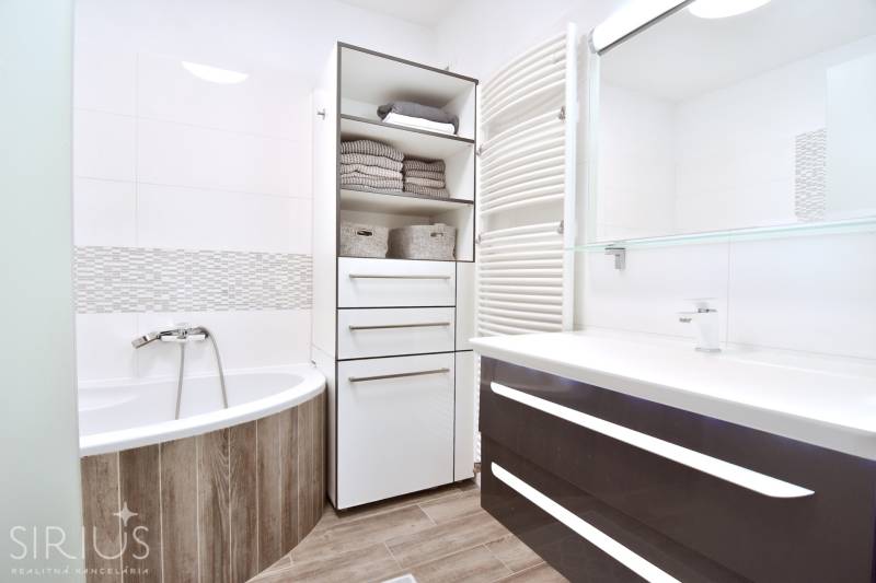 A bathroom with a bathtub, a wooden decor floor, and storage cabinets in a 3-room apartment.
