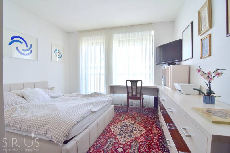 A bright bedroom with a chair, bed, and carpet in a 3-room apartment.
