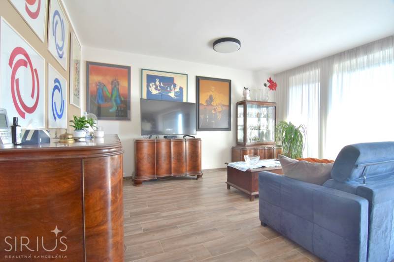 Living room with dark furniture, wood-patterned flooring, and decorative paintings in a three-room apartment.