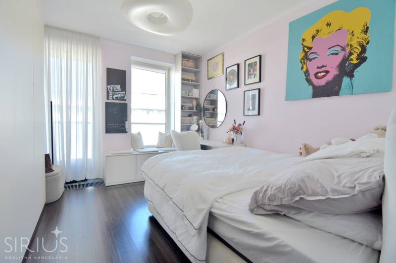 A bedroom in a three-room apartment with a wood-patterned floor and art paintings on the wall.