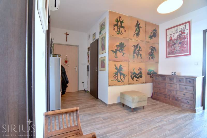 A hallway in a 3-room apartment with armchairs, paintings, and a wooden-patterned floor.