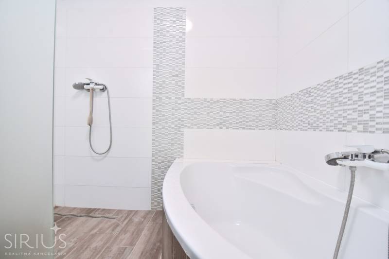 A bathroom with white tiles, a shower, a bathtub, and a wooden decor floor in a 3-room apartment.