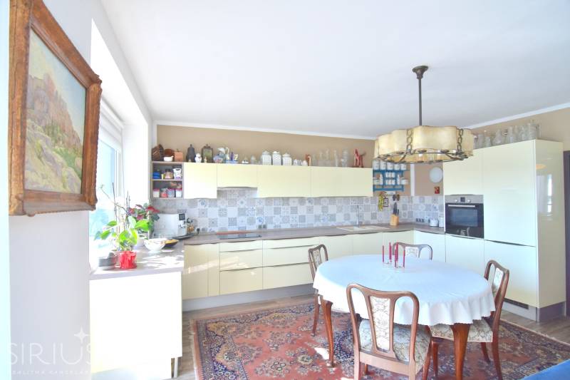 A kitchen in a 3-room apartment with wooden furniture, flowers, and a patterned carpet.