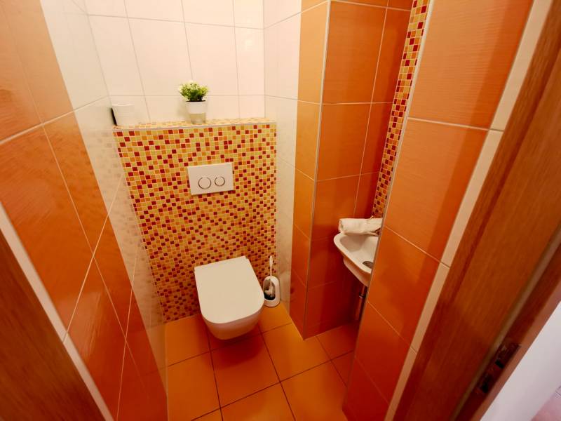 Toilet in a 4-room apartment with orange tiles and mosaic, small sink in the corner.
