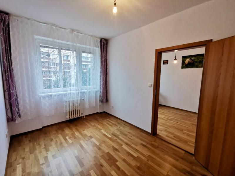 A room with a wooden decor floor in a 4-room apartment, light curtains on the window.