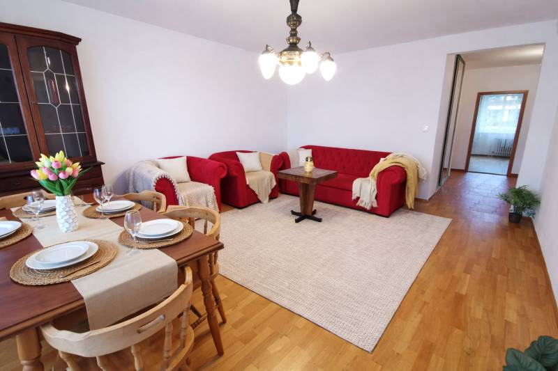 Living room in a 4-room apartment with red sofas, a dining table, and a wooden decor floor.