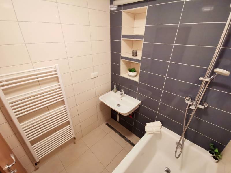 A bathroom in a 4-room apartment with a bathtub, a sink, and storage shelves.
