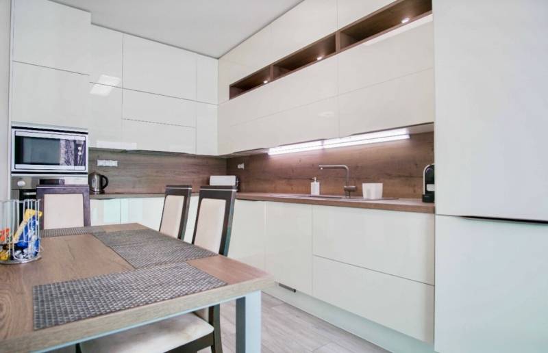 A kitchen in a 3-room apartment with glossy cabinets and wooden wall decor.