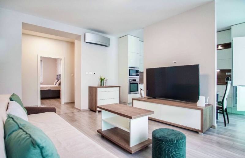 Living room in a three-room apartment with a wooden decor floor, a comfortable sofa, and a television.