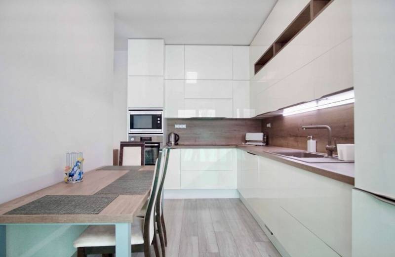 A kitchen in a 3-room apartment with a wooden decor floor and light furniture.