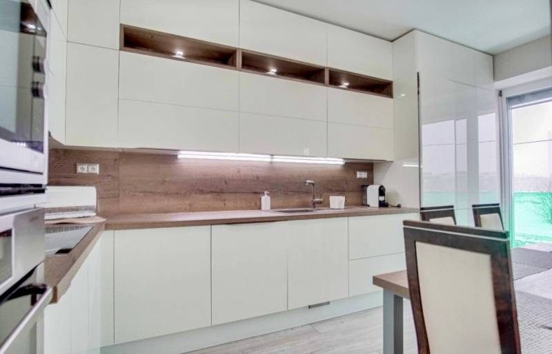 A kitchen in a 3-room apartment with white furniture and a floor with a wooden decor.