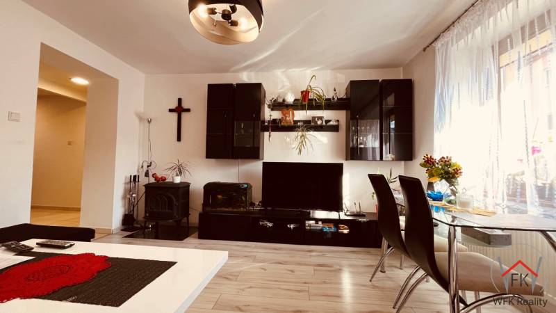 Living room of a three-room apartment with a wooden decor floor, dining table, and wall unit.