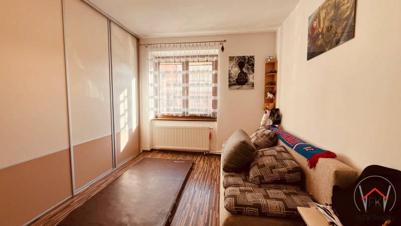 A room in a 3-room apartment with a wood-patterned floor, a sofa, and a built-in wardrobe.