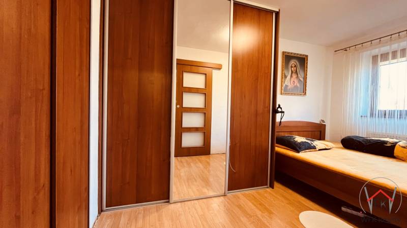 Bedroom in a 3-room apartment with wood-patterned flooring, a wardrobe, and a painting.