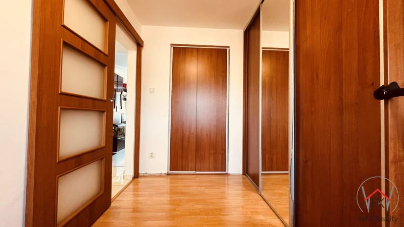 A hallway with a wardrobe and sliding doors, a floor with a wooden decor in a 3-room apartment.