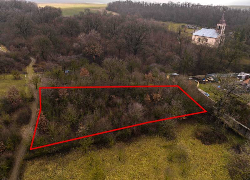 Recreational plots in Gemerské Teplice surrounded by trees with a historic church building in the background.