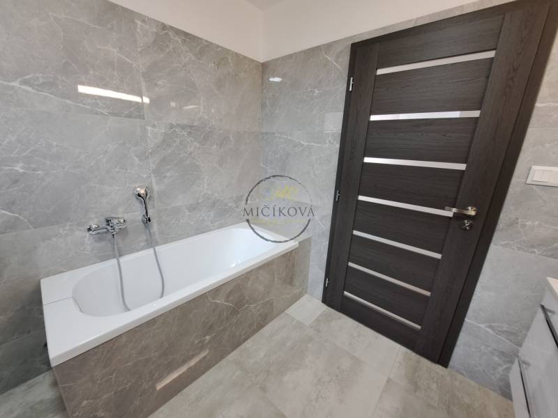 A bathroom in a family house with a bathtub, gray tiles, and dark doors.