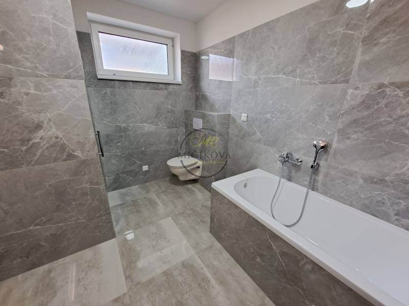 A bathroom with a bathtub and a toilet in a family house, tiled with gray tiles.