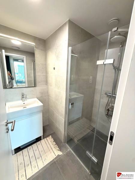 Bathroom in a 2-room apartment with a sink, shower corner, and decorative mat.