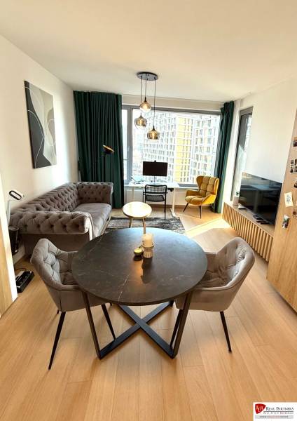 Living room with a sofa, dining table, and wood-patterned flooring in a two-room apartment.