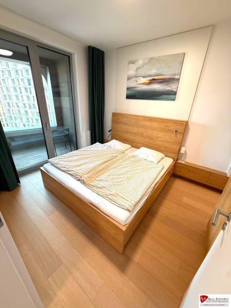 Bedroom in a 2-room apartment with a bed, balcony, and wooden decor flooring.