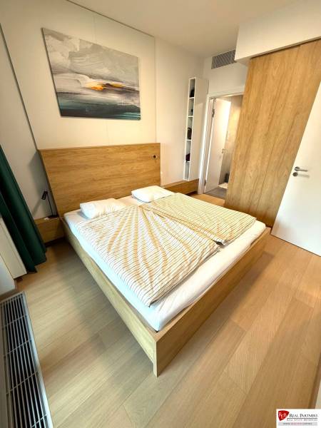 Bedroom in a two-room apartment with a wooden decor floor and a picture above the bed.